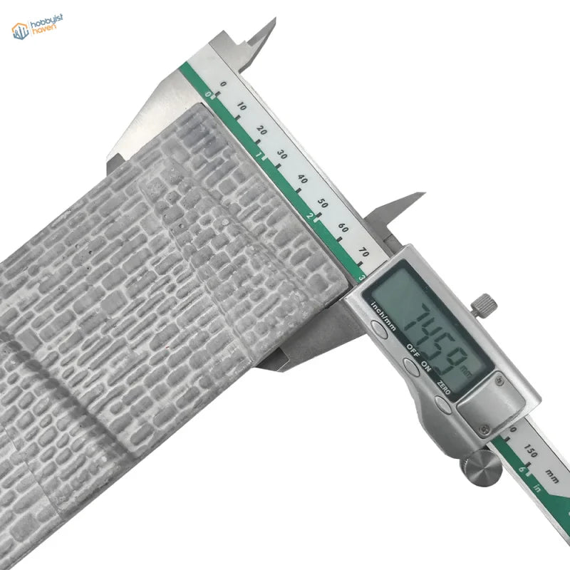 Silver digital caliper measuring gray metallic n scale stone retaining wall with textured embossed brick pattern