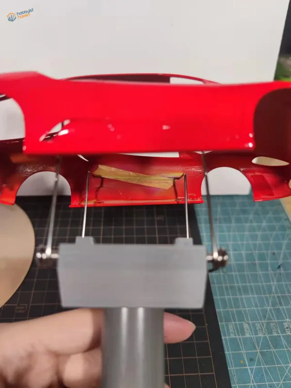 Red glossy plastic car model body held by gray rotating holder tool