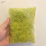 Hand holding clear bag of vibrant artificial green moss for scale model trees