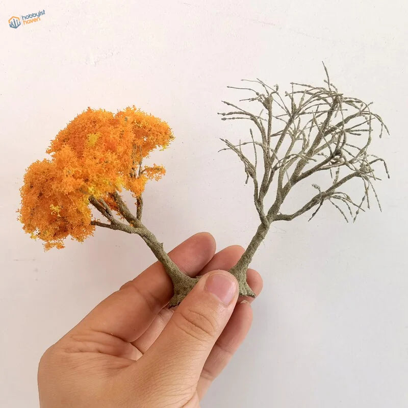 Hand holding scale model trees with orange mossy foliage and gray branches