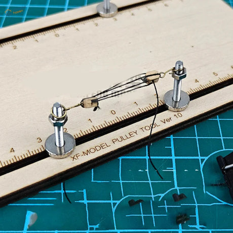 Silver metal ship model pulley block fixator tool with threaded bolts mounted on wooden ruler marked xf-model pulley tool ver 10