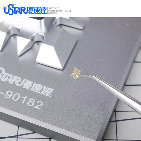 Gold grid-patterned microchip held by tweezers in UStar photoetch bending tool