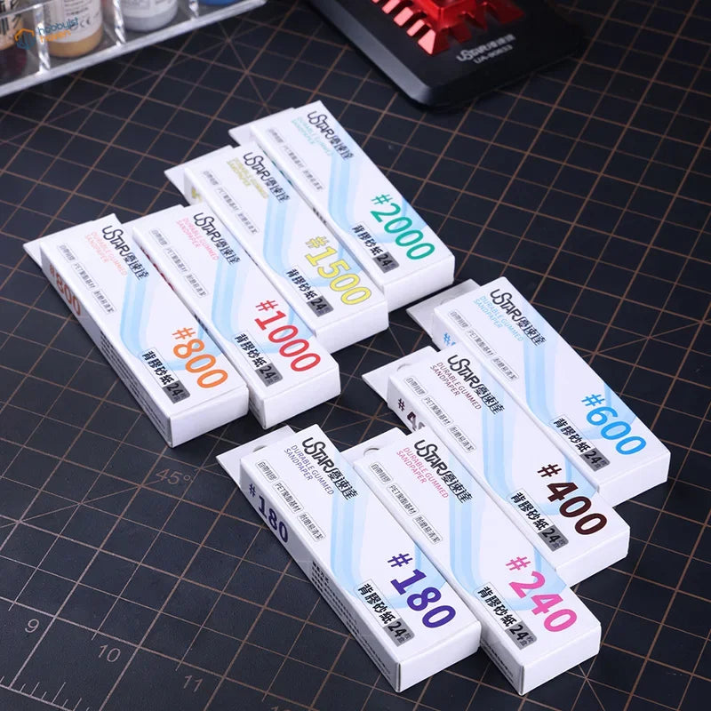 White rectangular uspap brand self-adhesive sandpaper sheets with colored grit labels and blue diagonal stripes for modeling use